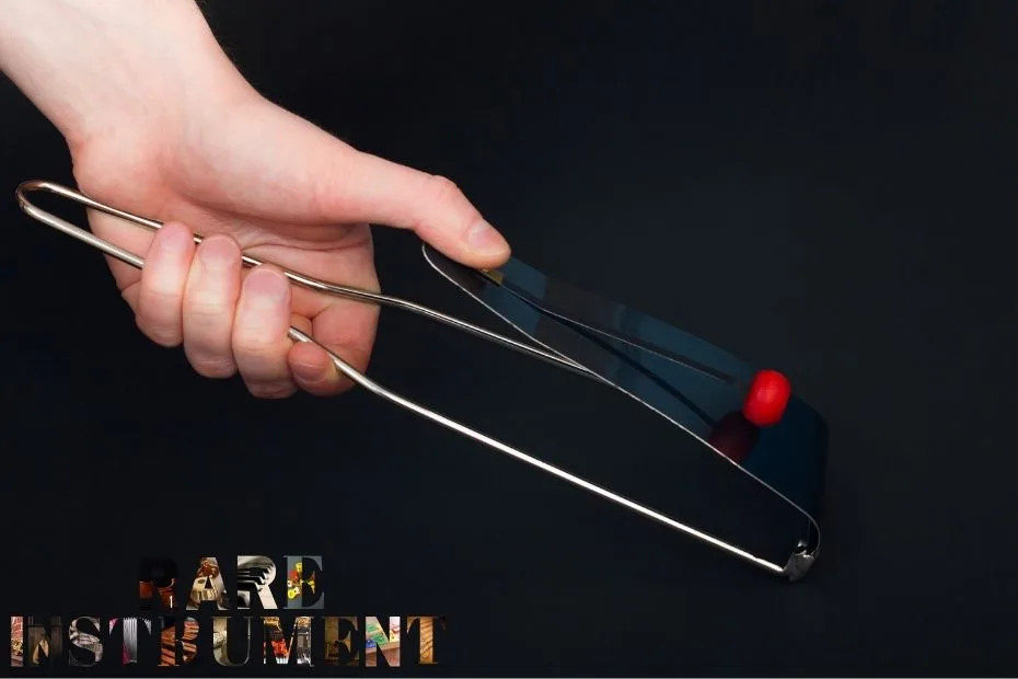 A hand holds a black flexatone with a red ball at the end, used for vibrato sounds.